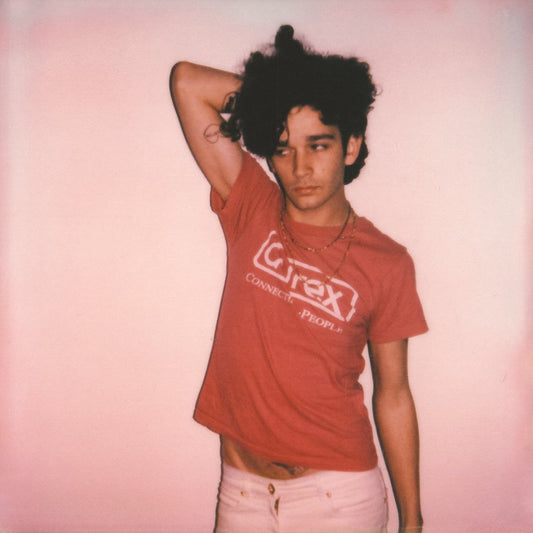 Man with curly hair in a red t-shirt against a pink background.
