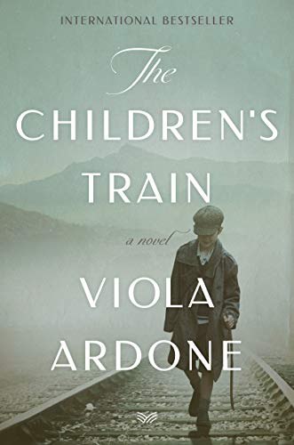 A young boy in a coat and cap walks along train tracks toward mountains.