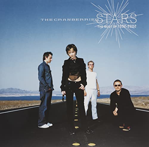The Cranberries band members stand on a desert road under a blue sky.