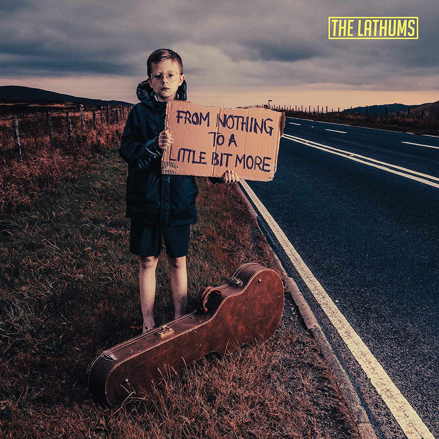 "CD album cover featuring a young boy holding a cardboard sign on a roadside."