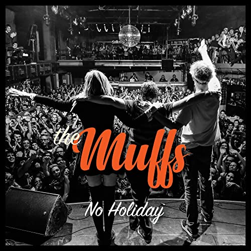 The Muffs band performing onstage before a large, crowded audience.