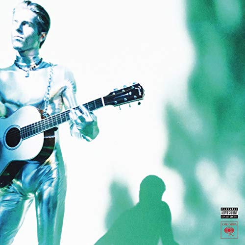 A person painted silver plays an acoustic guitar against a bright, green-tinted background.