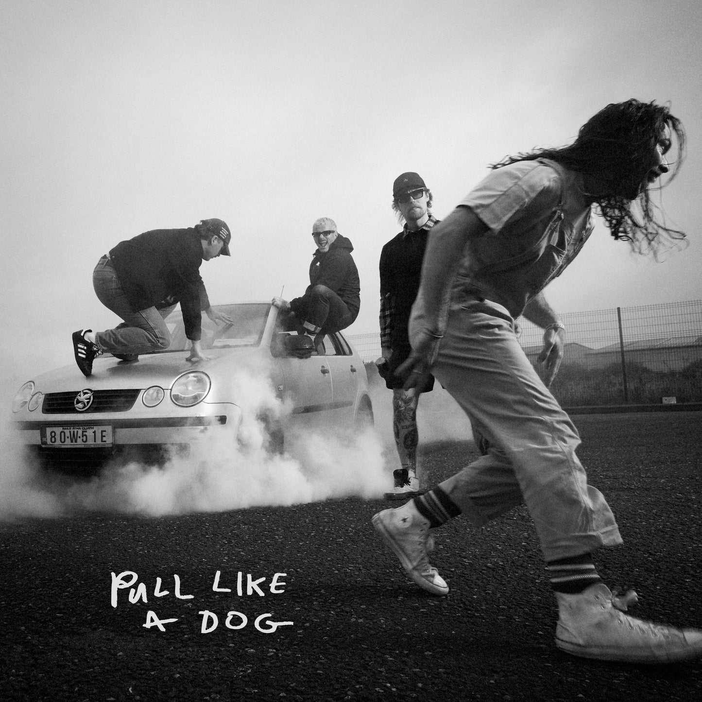 Black and white album cover featuring a band with a car doing a burnout.