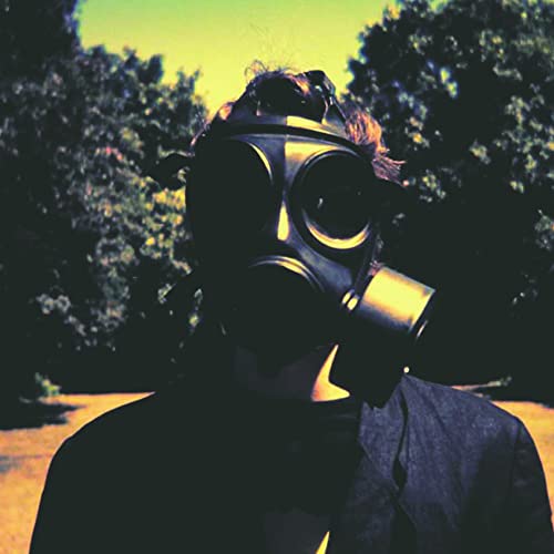 Person wearing a black gas mask, trees blurred in background.