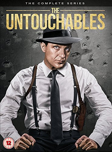 A man in a fedora, white shirt, and tie stands against a bullet-riddled wall.