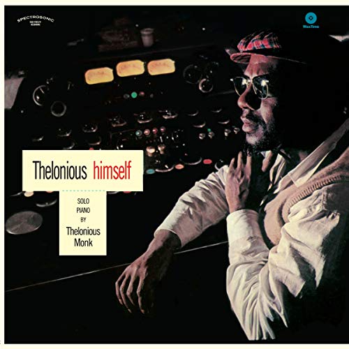 Thelonious Monk wearing a cap and glasses in front of a recording studio console.