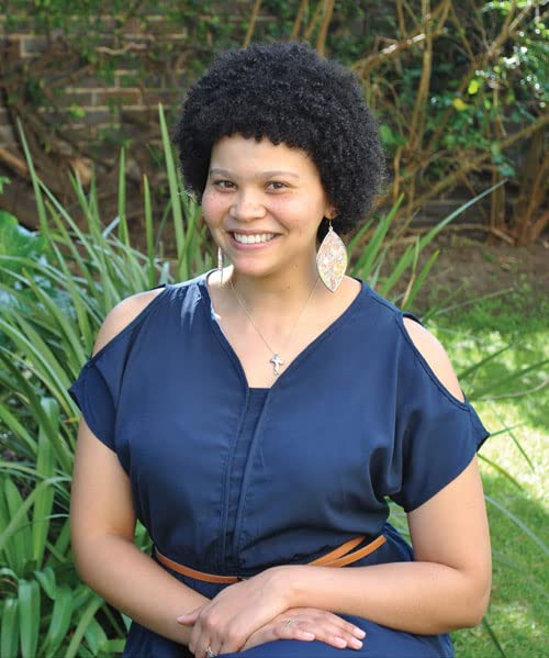 Smiling woman with short curly hair, wearing a dark blue dress.