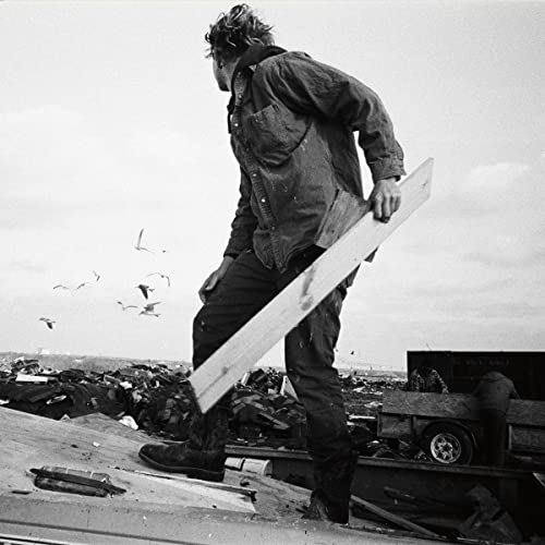 Black and white photo of a man carrying a long white board.