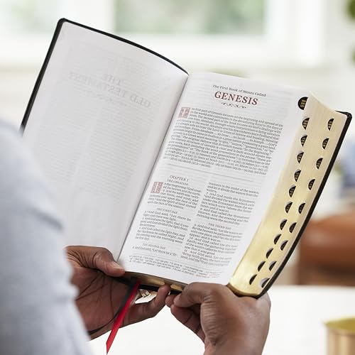 Open black Bible with red lettering and gold-edged pages, held by hands.