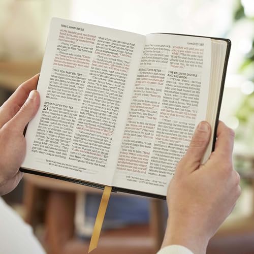 Open purple Bible with large print and red lettering held by two hands.