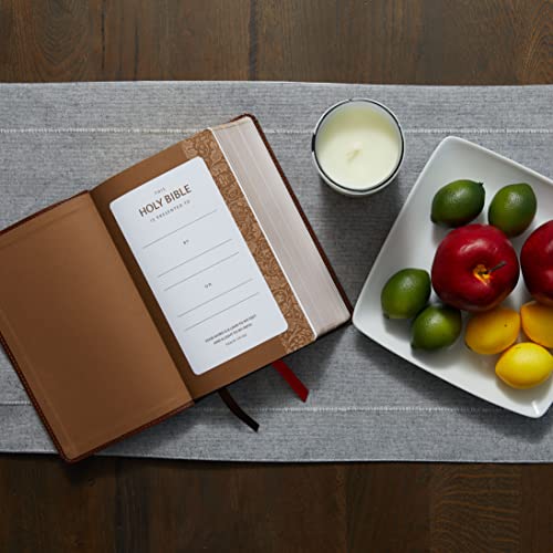 Open brown leather Bible with presentation page, candle, and fruit nearby.
