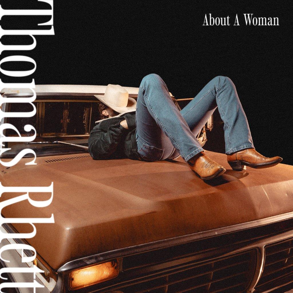 A man in a cowboy hat and jeans lying on the hood of a truck.
