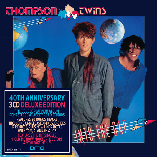 The three members of Thompson Twins stand against a blue background with globes.