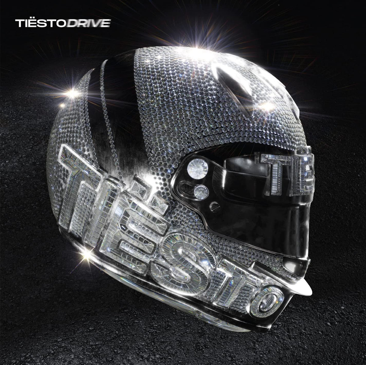 "Silver motorcycle helmet with 'Tiësto' written on it, covered in rhinestones, on a black background."