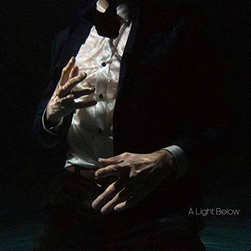 A person in a suit and white shirt with hands raised against black background.