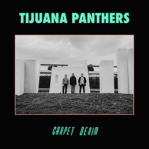 "Album cover with three men standing in front of white structures, black background."
