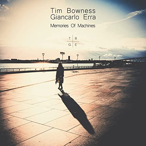 A lone figure walks along a paved waterfront at sunset with a long shadow.