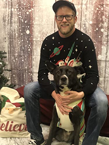 A man in a space-themed sweater holds a dog wearing a striped sweater.