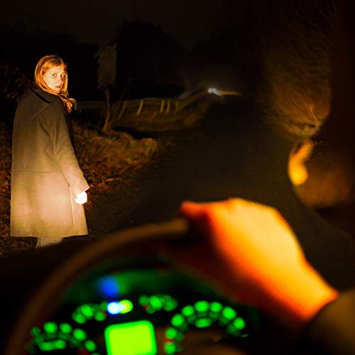 Woman standing by a road, viewed from a car dashboard.