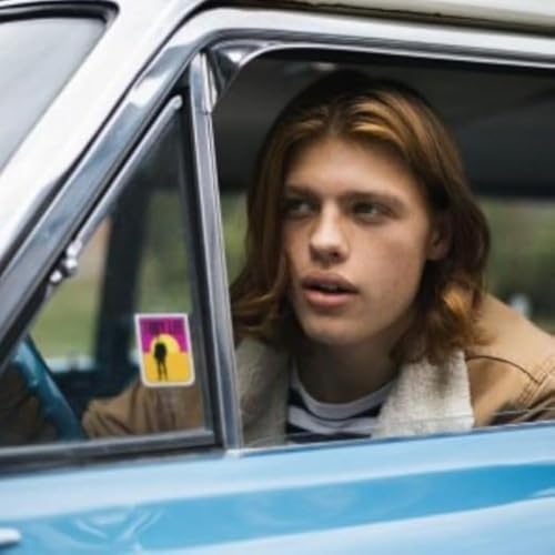 Young man with long hair looks out from a car window.