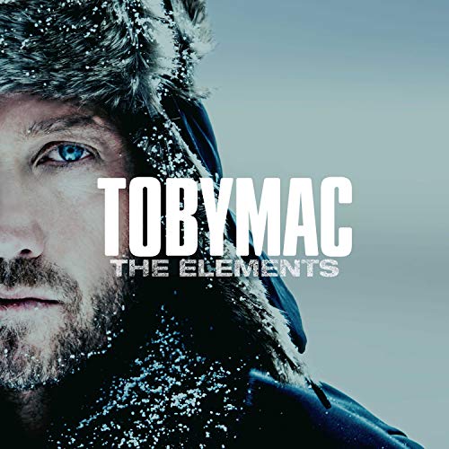 Man in winter clothing with snow on face and fur-lined hood, blue eyes visible.