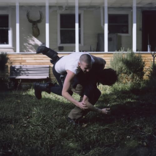 Two people grappling on a lawn in front of a house.