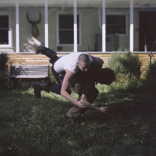 Two people wrestling on a lawn in front of a house with a porch.