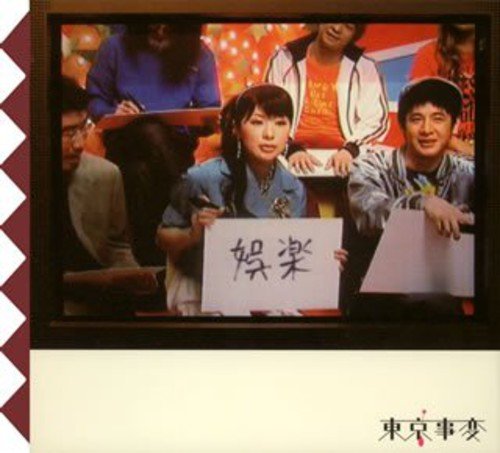 A woman holds a sign with Japanese characters in a television studio setting.