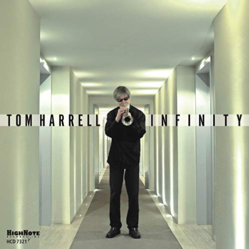 Tom Harrell stands playing trumpet in a long, white hallway.