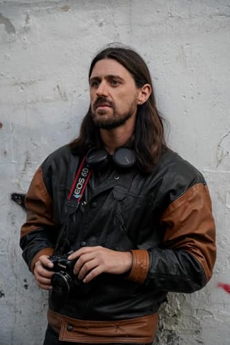Man with long hair holding a camera, wearing a leather jacket.