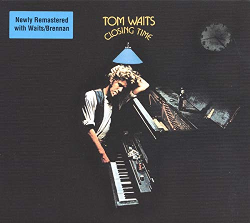 Tom Waits sitting at a piano under a blue lamp on a dark background.