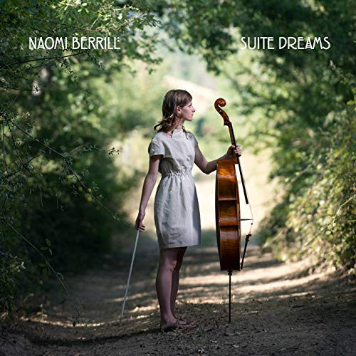 Woman with cello standing on a path surrounded by trees.