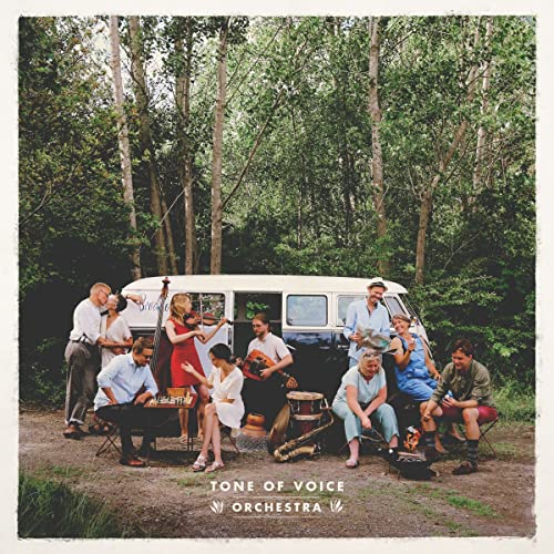 Group of musicians with instruments gathered around a vintage camper van.