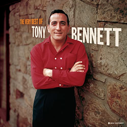 Tony Bennett wearing a red shirt, arms crossed, standing against a stone wall.