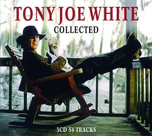 Tony Joe White sits in a rocking chair holding a guitar on a porch.