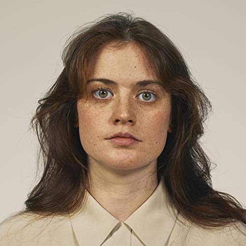 A close-up portrait of a woman with freckles and brown hair against a background.