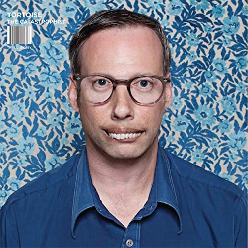 CD cover with a portrait of a man wearing glasses, blue floral background.