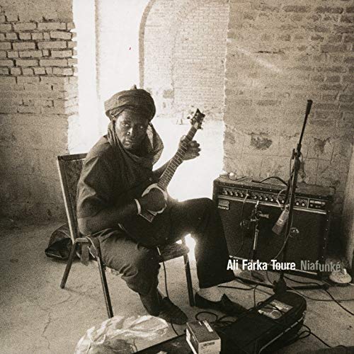 Ali Farka Touré playing an acoustic guitar while sitting in a rustic brick room.