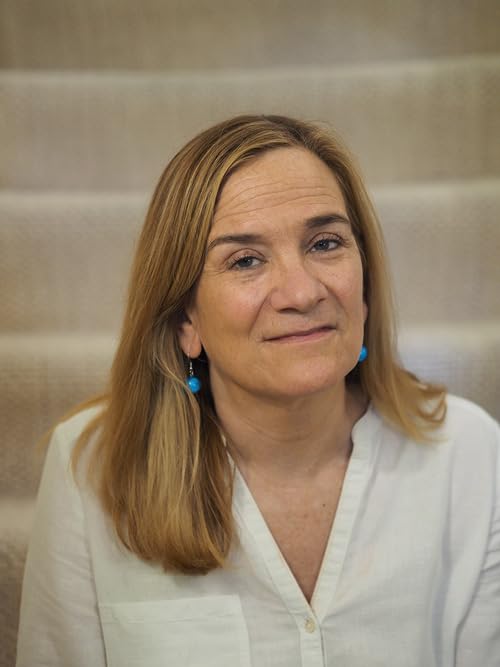A middle-aged woman with shoulder-length blonde hair wearing a white shirt and blue earrings.