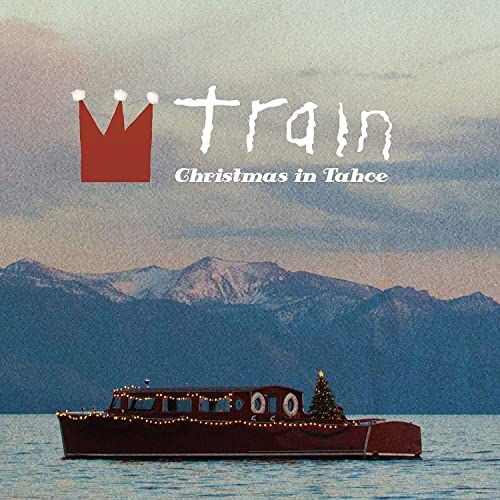 A boat decorated with Christmas lights floats on a lake before mountain peaks.