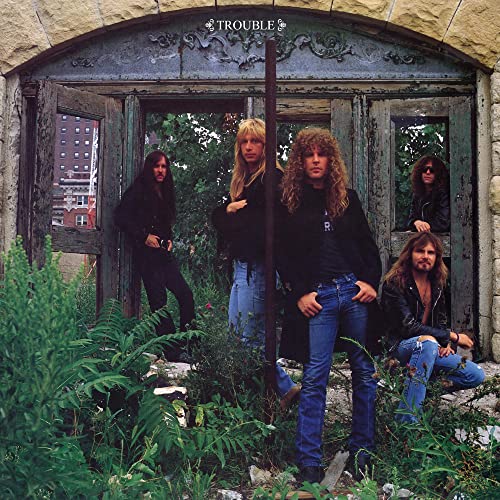 Five long-haired men in black clothing posing in front of a rustic stone doorway.
