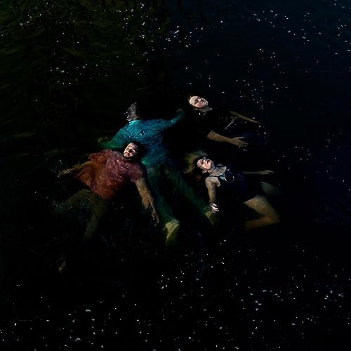 Three people float in dark water, looking upwards at the sky.