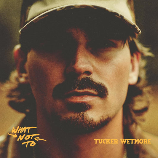 Close-up portrait of Tucker Wetmore wearing a cap, with album title and artist name.