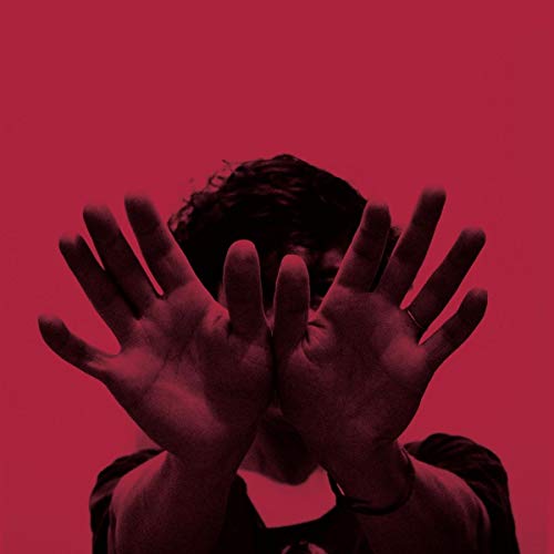Person with hands obscuring face against a solid red background.