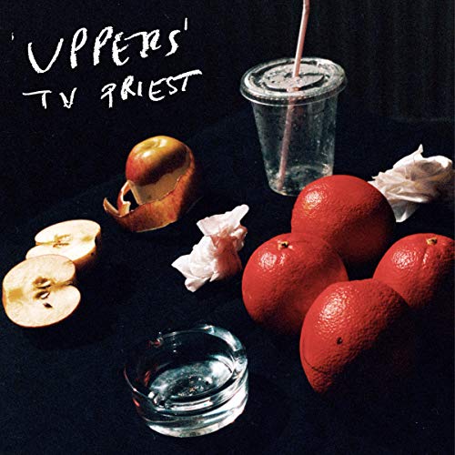 "Album cover with sliced fruit, crumpled paper, and glasses on a dark background."