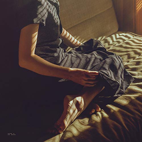 Person in a patterned dress sitting on a bed with striped sunlight shadows.