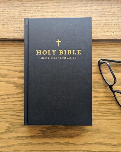 Black Bible with gold lettering and a cross, resting on wood.