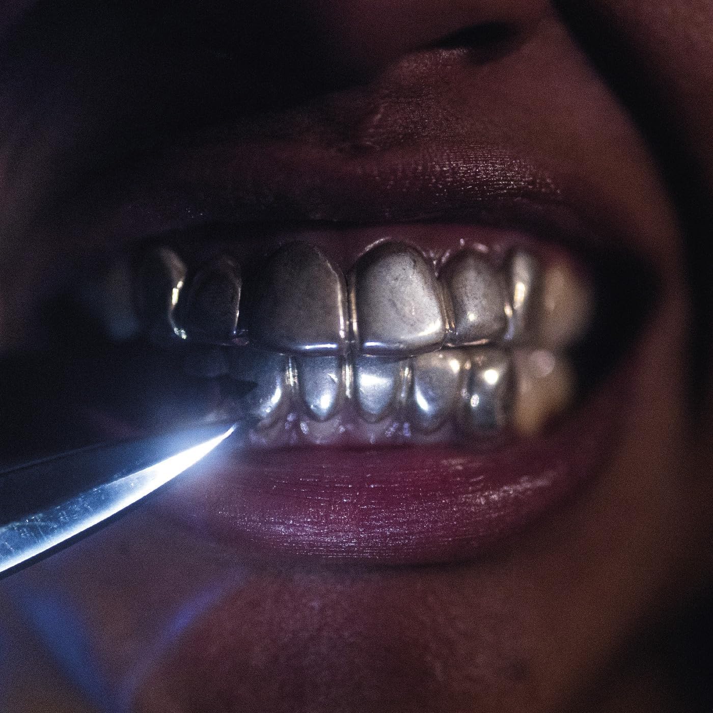 Close-up of a person with silver grillz and a lit blue object.