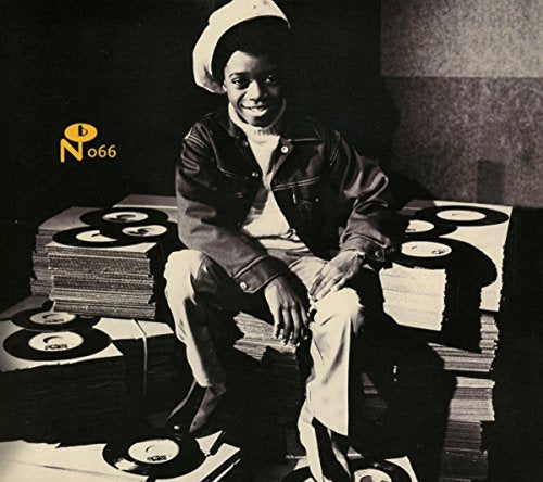 A young boy in a hat sits surrounded by stacks of vinyl records.