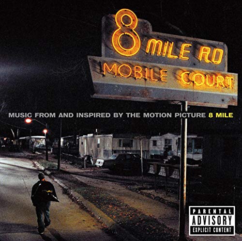 A person walks down a dark street toward an illuminated 8 Mile Road sign.